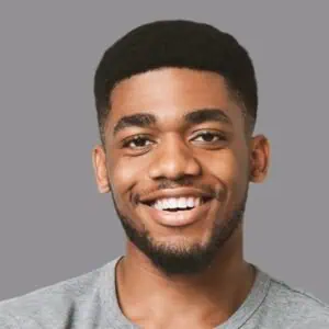Smiling young man with short black hair and beard, gray background.